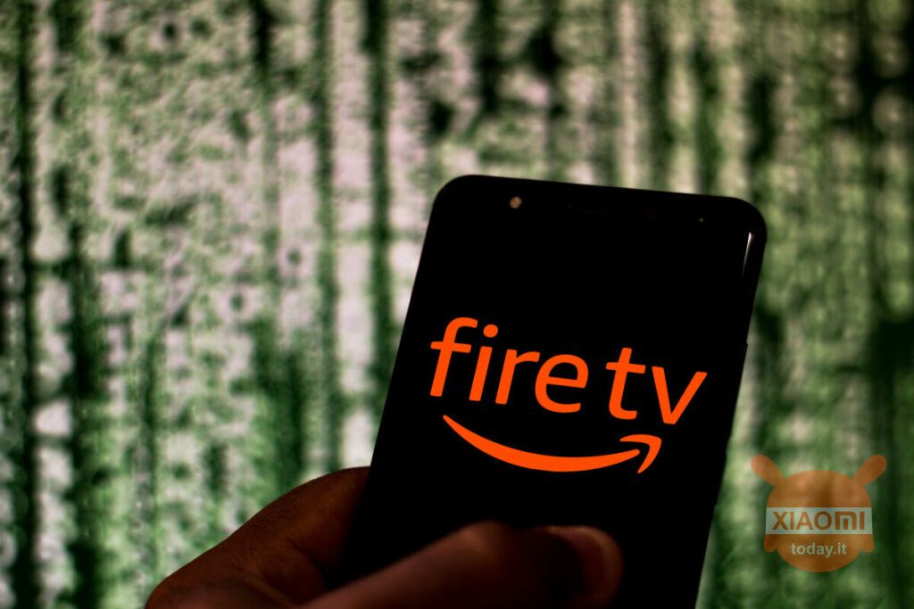 Smartphone con schermo che visualizza il logo di Fire TV, tenuto in mano con uno sfondo sfocato di codice digitale verde.