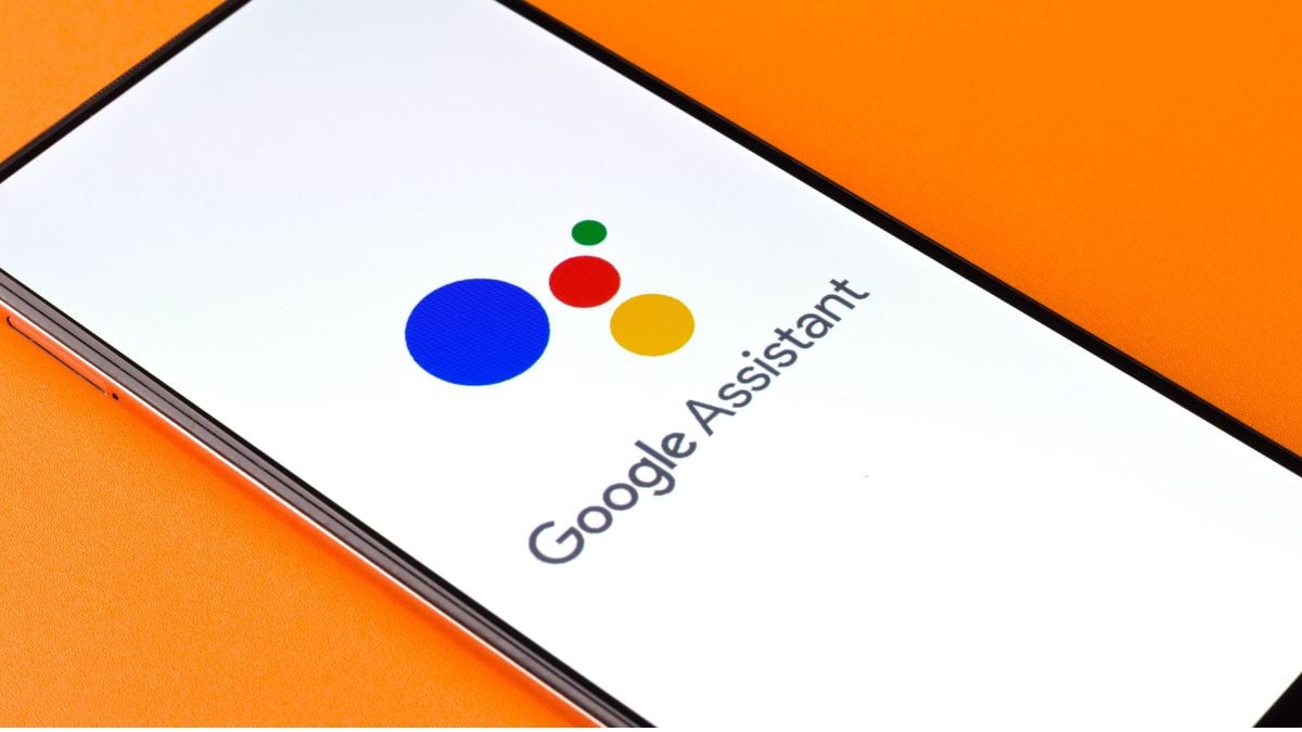 गूगल असिस्टेंट लोगो वाला स्मार्टफोन। डिवाइस नारंगी पृष्ठभूमि पर स्थित है